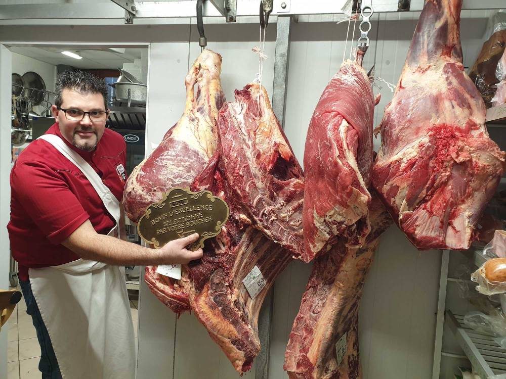 Artisan boucher tenant une plaque d'excellence devant des morceaux de boeuf